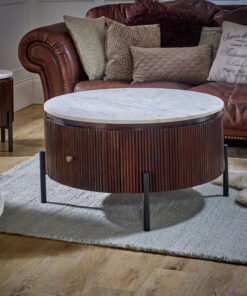 Opal Mango Wood round coffee table with a white marble top and fluted dark brown base, supported by black metal legs in a living room with a brown leather sofa and patterned cushions.