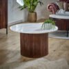 Round Opal Mango Wood Coffee Table with Marble Top featuring a ribbed dark brown base in a stylish living room with plants and a leather chair